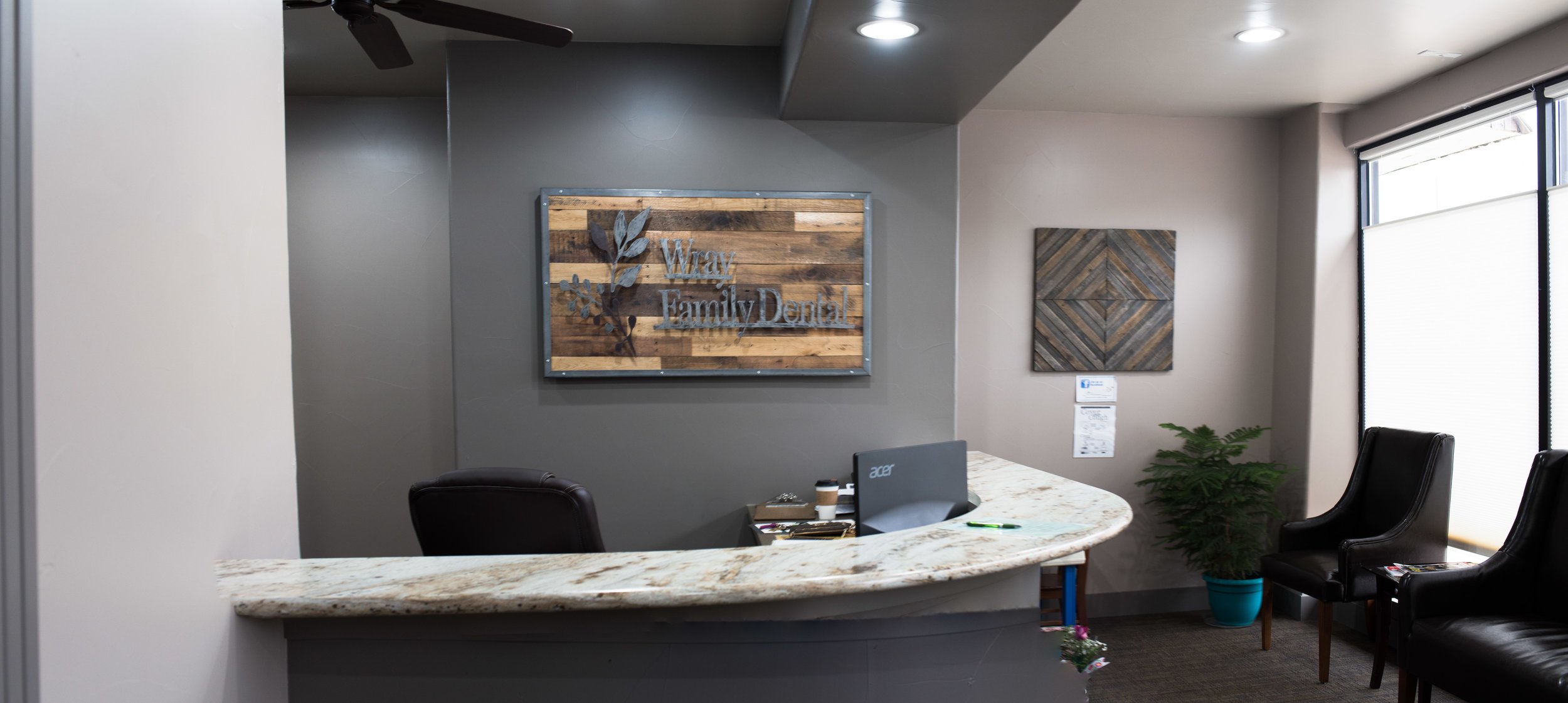 Front desk and waiting area at Wray Family Dental with a wood practice sign on the wall